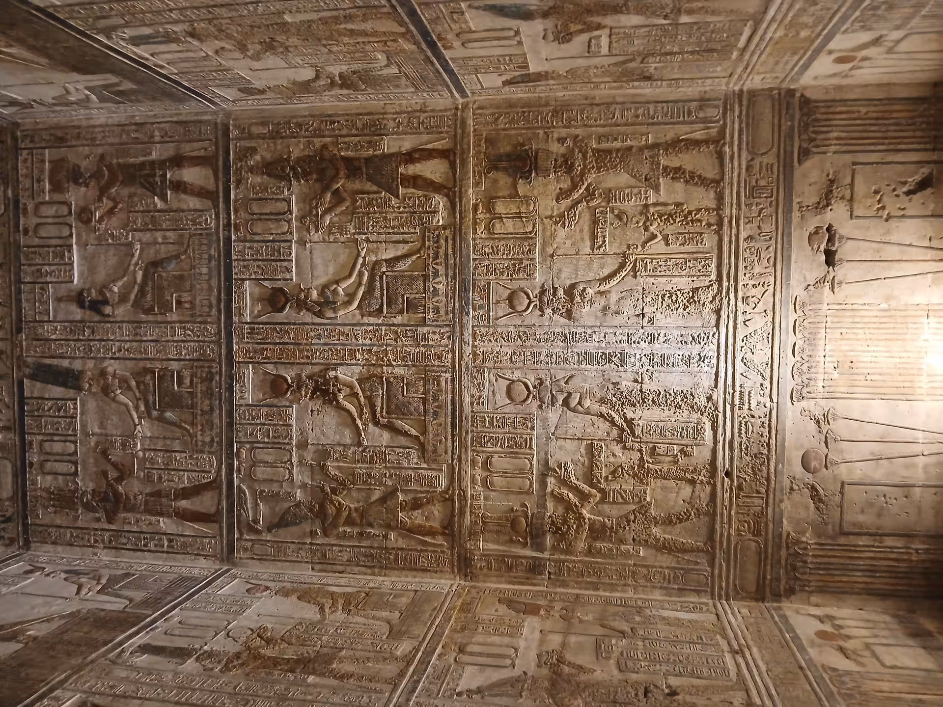 Ancient Egyptian temple ceiling adorned with detailed carvings and hieroglyphics depicting historical scenes.