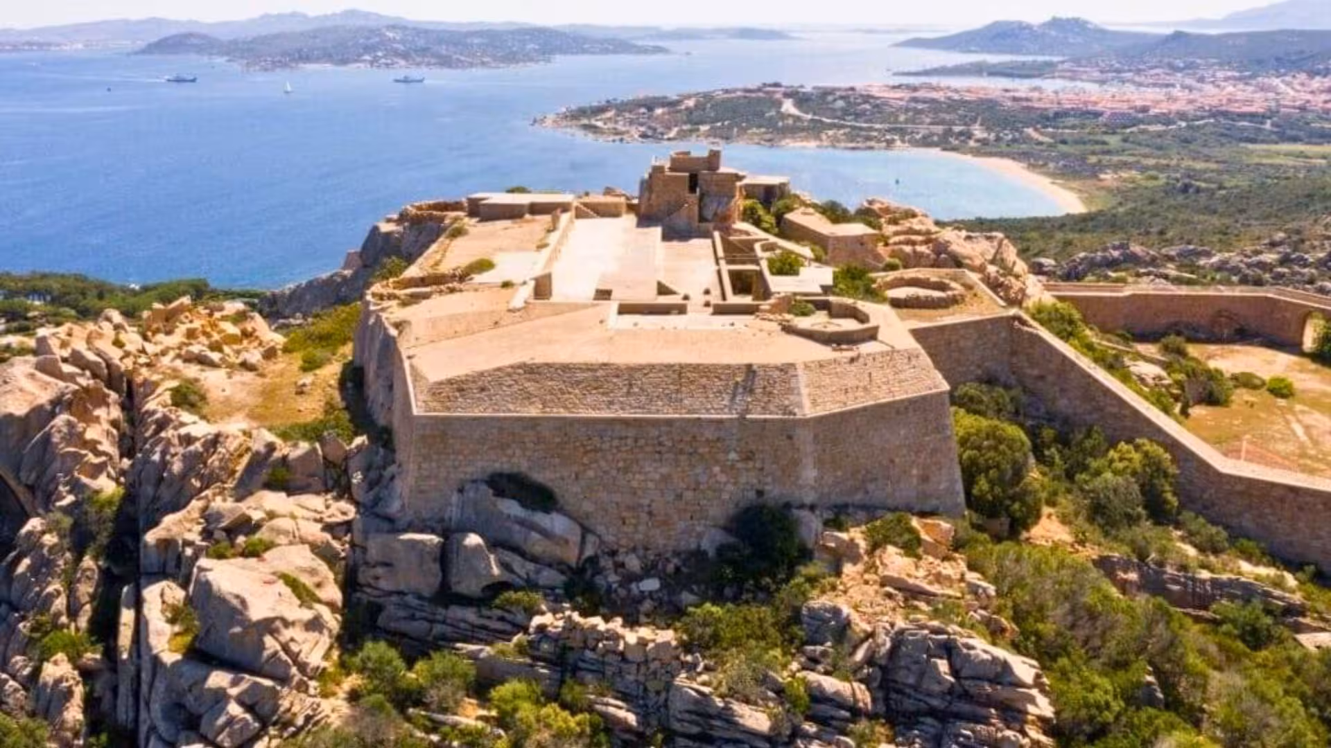 Panoramic view of ancient fort atop rocky cliffs with stunning sea backdrop in La Maddalena, ideal for history tours.