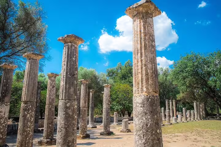 Ancient columns under a bright blue sky at the Archaeological Site of Olympia in Greece.