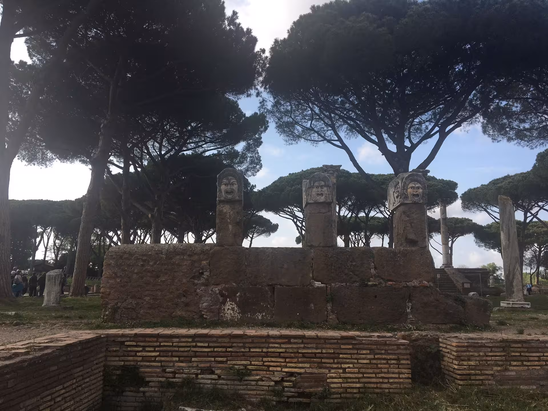 Ancient Ostia ruins with carved stone faces amidst pine trees on a Fiat '500 vintage tour.
