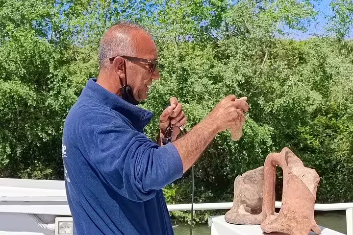 Guide on Ancient Ostia river cruise from Rome explaining Roman artifacts on deck against lush Tiber River scenery