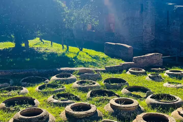 Row of ancient Roman storage jars in grassy courtyard at Ostia Antica, explored on guided boat and walking tour from Rome
