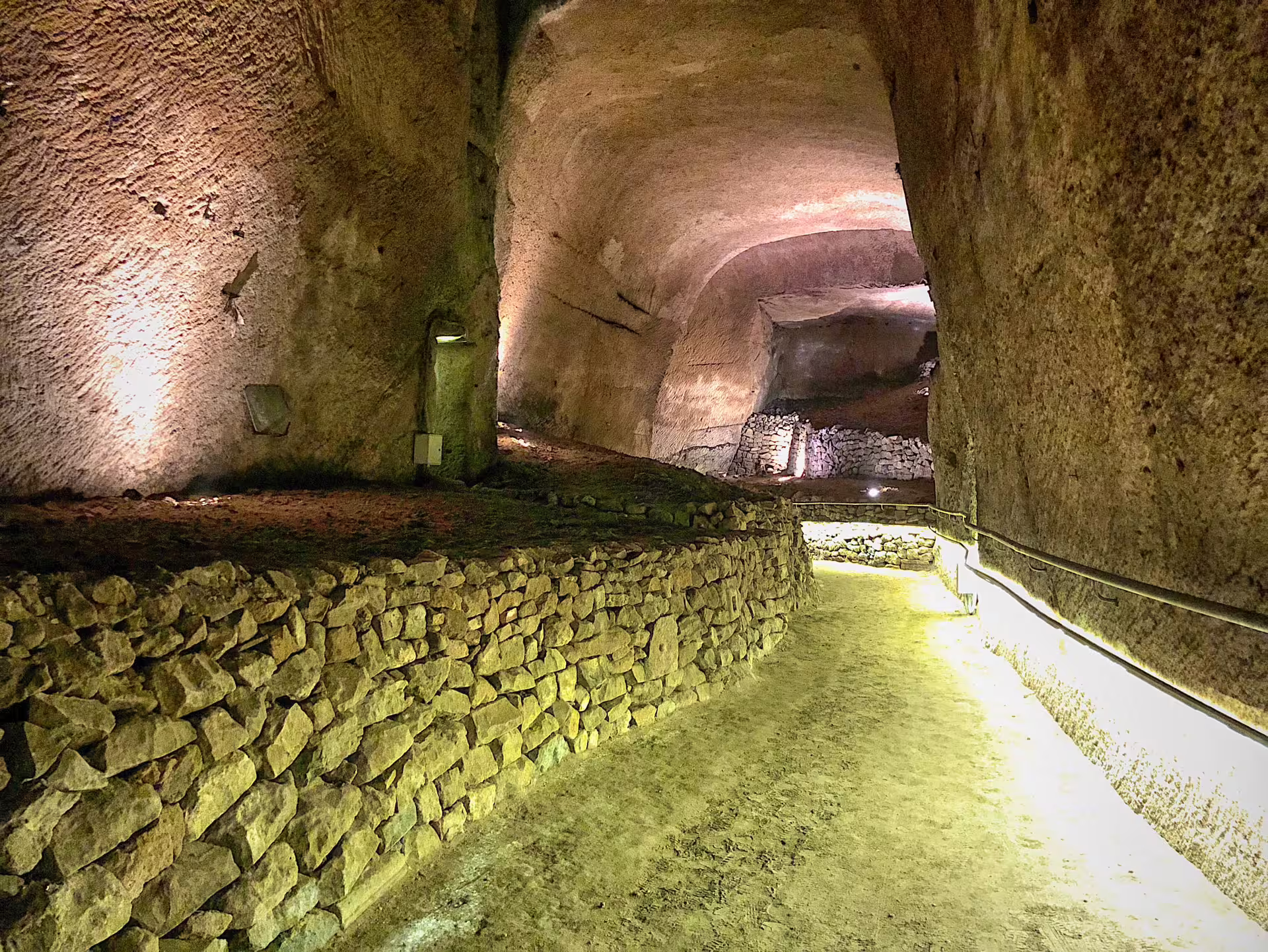 Ancient stone tunnel and lit pathway in the Naples underground on the L'Inferno di Dante al Decumano Sommerso experience