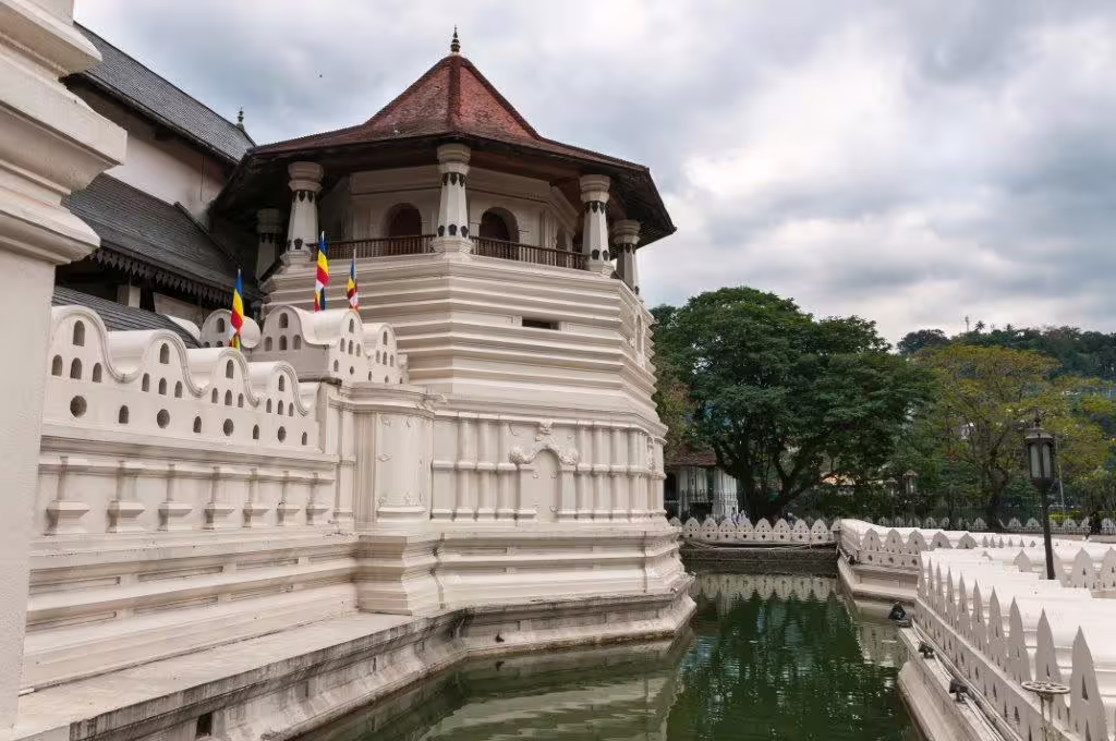 Majestic ancient temple with intricate white architecture reflecting in a peaceful moat under a cloudy sky.