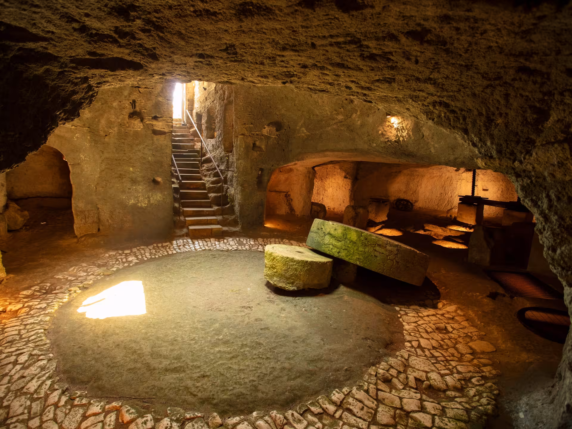 Ancient underground olive mill near Otranto featuring stone grinding wheels and cobbled floor.