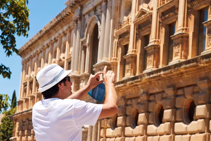 Tourist capturing the stunning Renaissance architecture of a historic building in Andalusia under a clear blue sky.