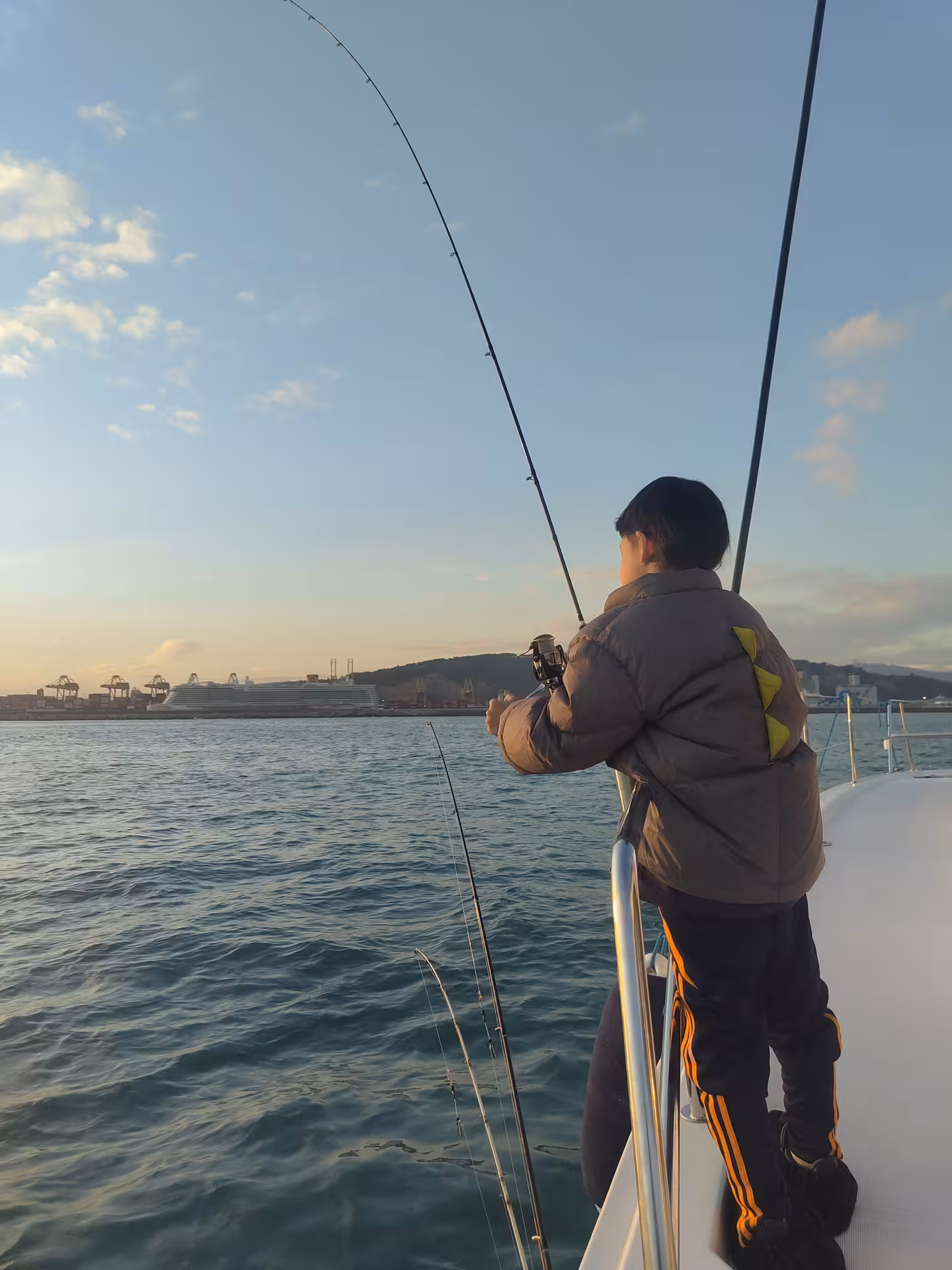 Angler casting from a boat at sunset on the Mediterranean Sea, guided fishing charter with coastal views