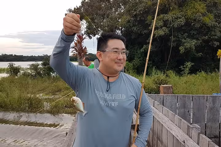 Angler holds a caught piranha on a wooden dock during Solimões River Amazon piranha fishing tour