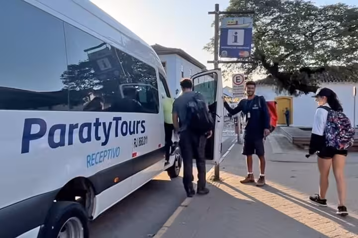 Group of tourists posing in front of Paraty Tours vans with a church backdrop in Angra dos Reis at sunset.