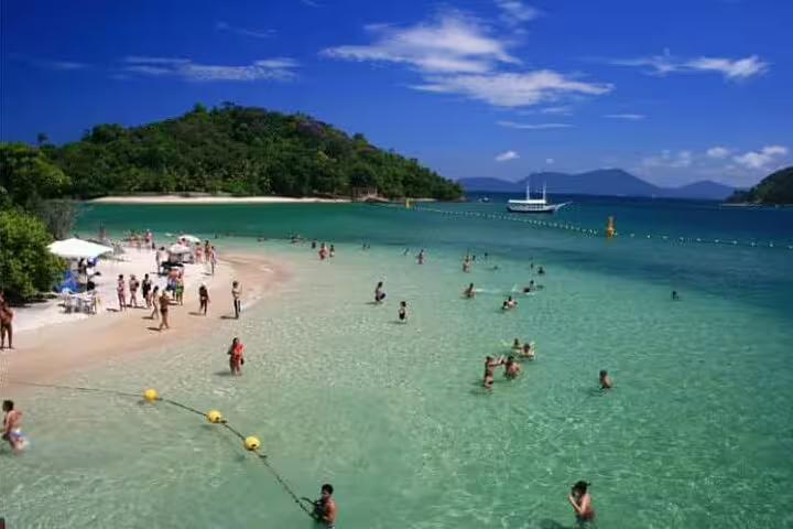 Tourists relaxing on pristine beach with turquoise waters and lush greenery on Angra & Ilha Grande boat tour.