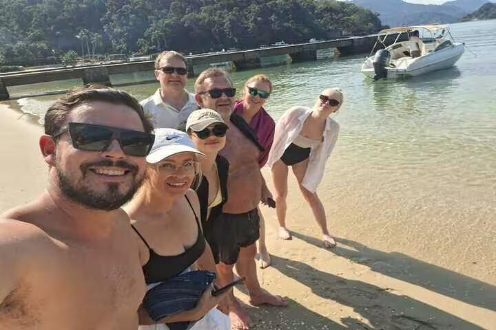 Happy tourists on sandy beach at Isla Grande with boat ready for Angra & Ilha Grande BBQ tour from Rio.