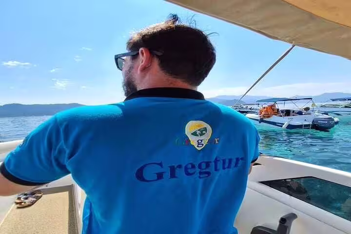 Tour guide steering a boat on the Angra & Ilha Grande tour, showcasing vibrant waters and scenic island views.