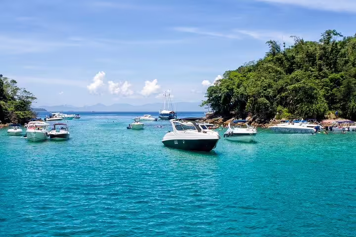 Boats anchored in crystal-clear waters surrounded by lush greenery on an Angra & Ilha Grande private boat tour.