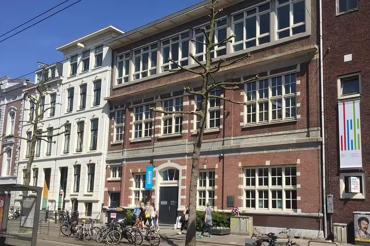 Historic building in Amsterdam's Jewish Cultural Quarter on a sunny day, featuring visitors and bicycles, part of the Anne Frank Walking Tour.