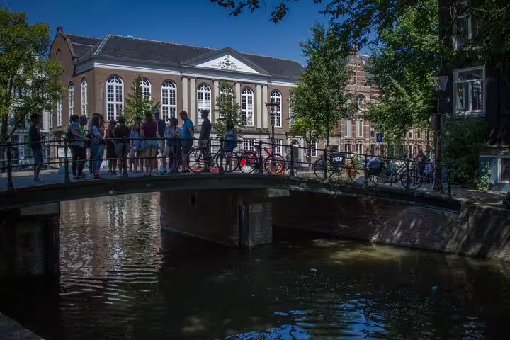 A group of tourists stands on a picturesque canal bridge in Amsterdam's Jewish Cultural Quarter during the Anne Frank Walking Tour.