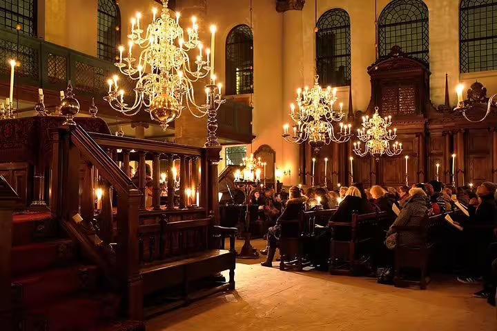 People gathered in a historic synagogue, illuminated by chandeliers, during the Anne Frank Walking Tour in Amsterdam's Jewish Cultural Quarter.