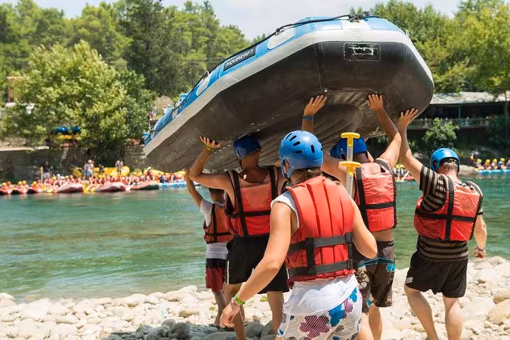 Rafting team carrying inflatable boat to the river for Antalya rafting tour with helmets and life vests