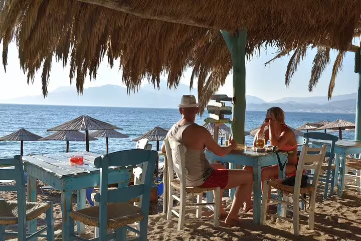 Tourists enjoying a seaside meal under a thatched canopy overlooking the Mediterranean in Apokoronas, Crete.