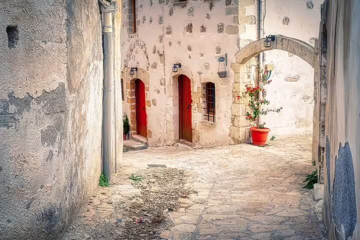 Charming stone alley in Apokoronas village with red doors and flowering plants, ideal for a private Crete tour.