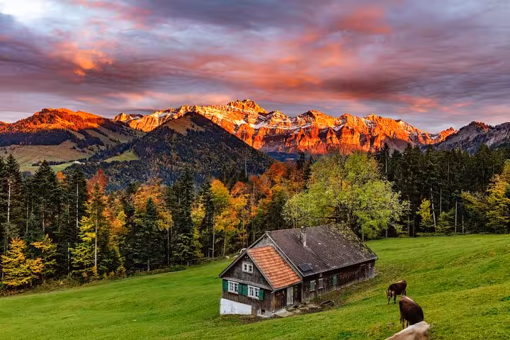 Scenic view of Appenzell's autumn landscape with a rustic farmhouse and Alps at sunset, ideal for cultural and cheese tours.