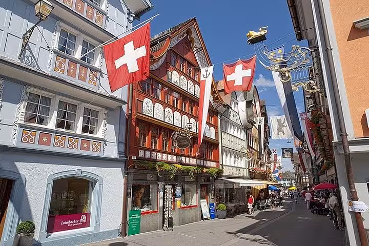 Colorful Swiss flags and historic architecture line a bustling street in the heart of Appenzell, Switzerland.