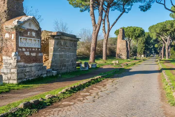 Ancient tombs and pine trees line the historic Appian Way near Rome, a peaceful stop on a guided catacombs and underground tour