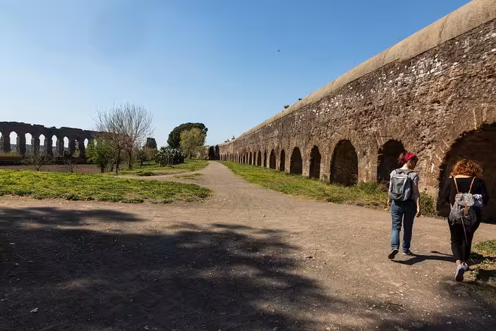 Two people walking by ancient Roman aqueduct ruins on the historic Appian Way e-bike tour.