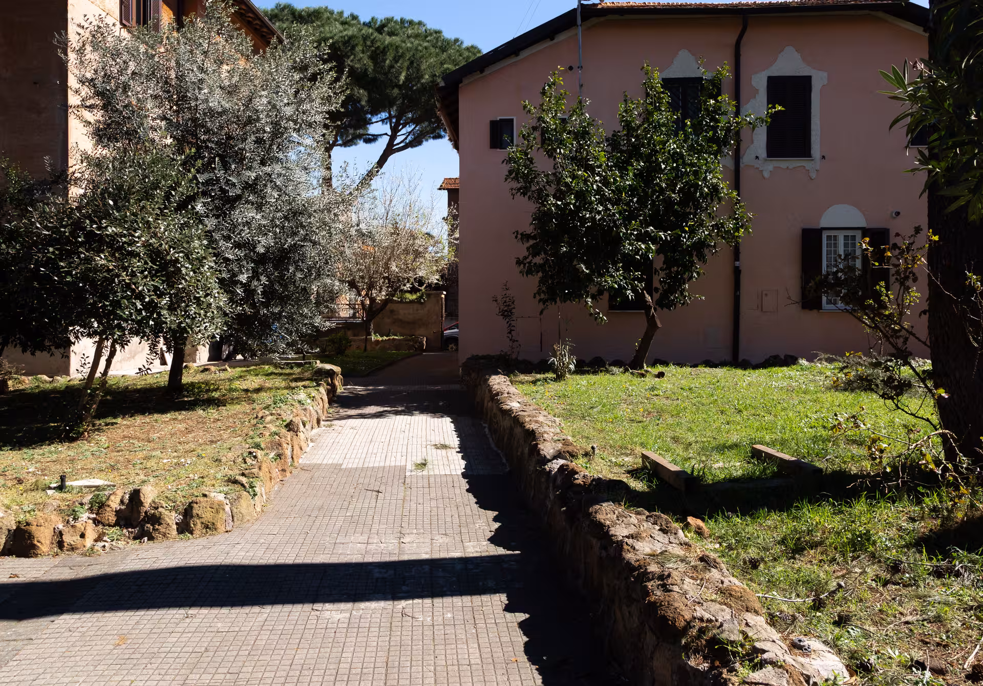 Charming path leading to a rustic pink house surrounded by lush greenery on the Appian Way tour.