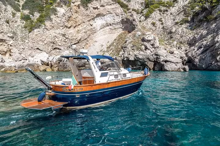 Gozzo Apreamare 10 cruising clear waters near rocky cliffs on Sorrento to Capri private boat experience.