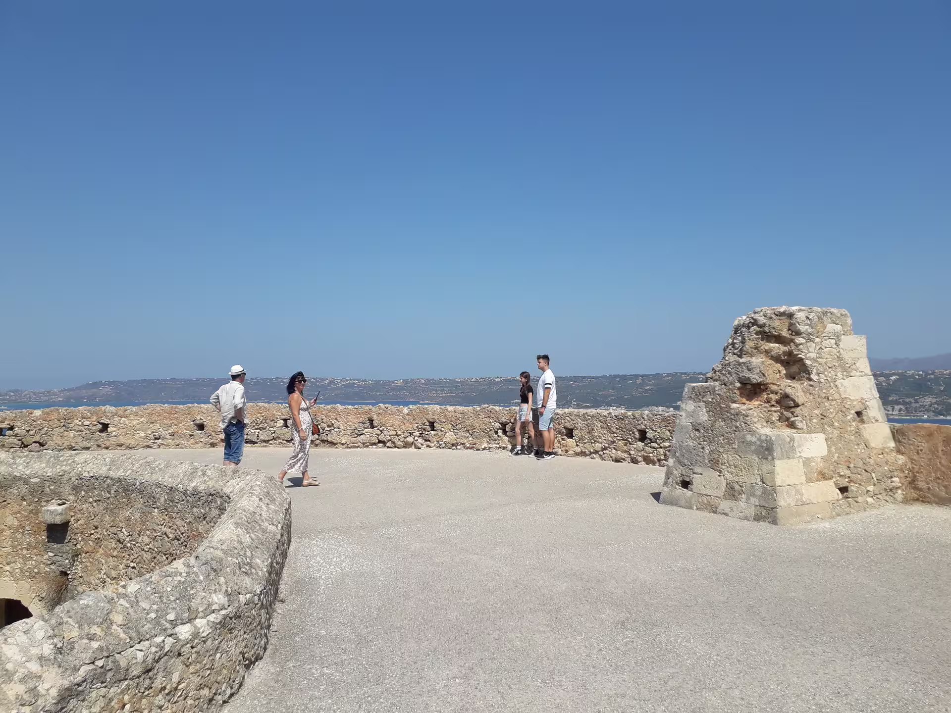 Visitors walking along ancient stone walls with panoramic views at Aptera archaeological site.