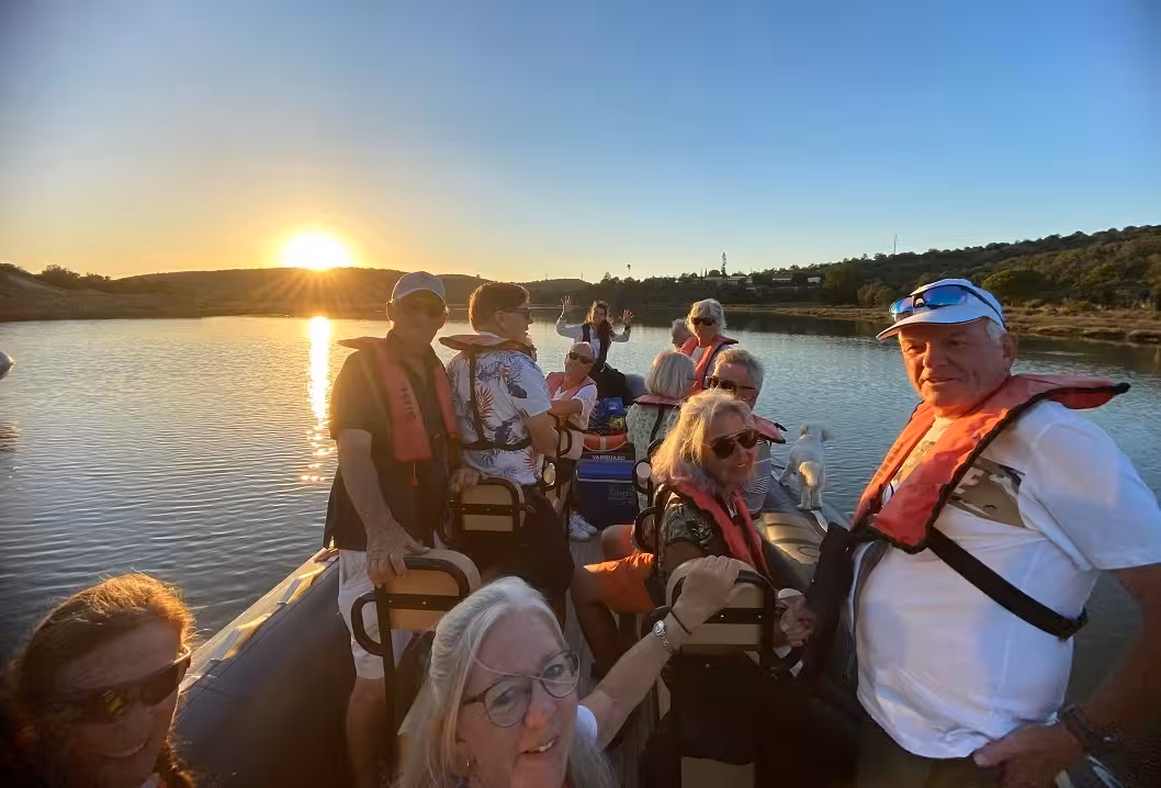 Group of adults wearing life jackets enjoy a golden sunset cruise on the Arade River during a scenic Silves boat tour