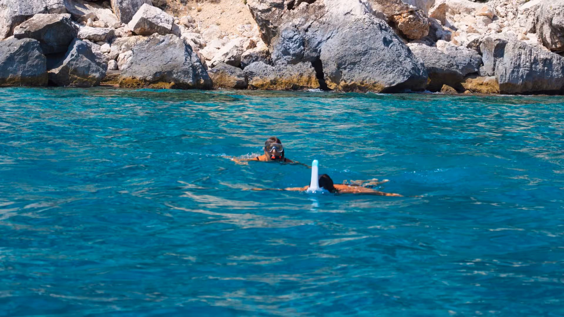 Snorkelers exploring crystal-clear waters near rocky shores on Arbatax RIB trip between Cala Luna and Cala Goloritzé.