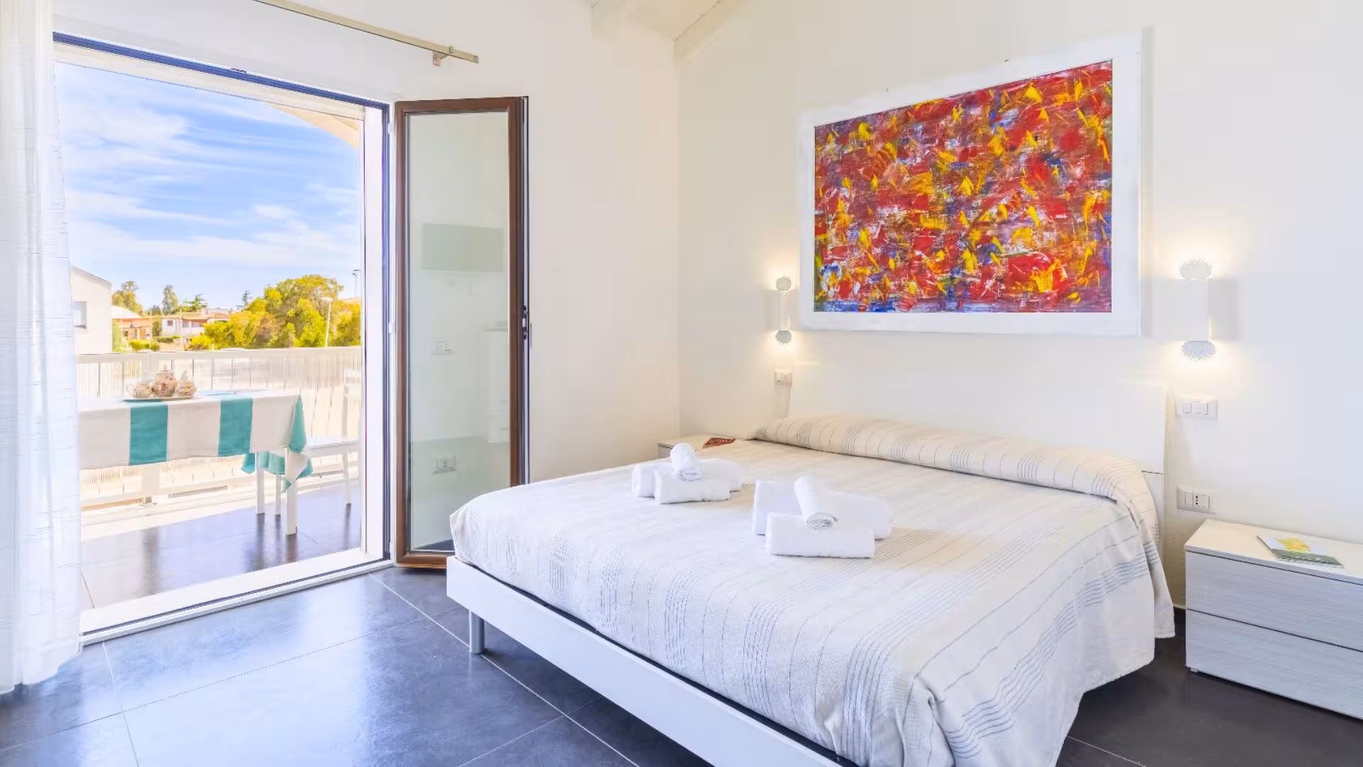 Bright and airy bedroom with modern decor, balcony view, and vibrant art, available on the Selvaggio Blu trek from Arbatax.