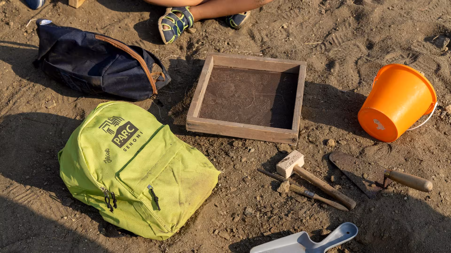 Archaeology tools and vibrant backpack on sandy ground, ready for exploration at Giara Park, Genoni.