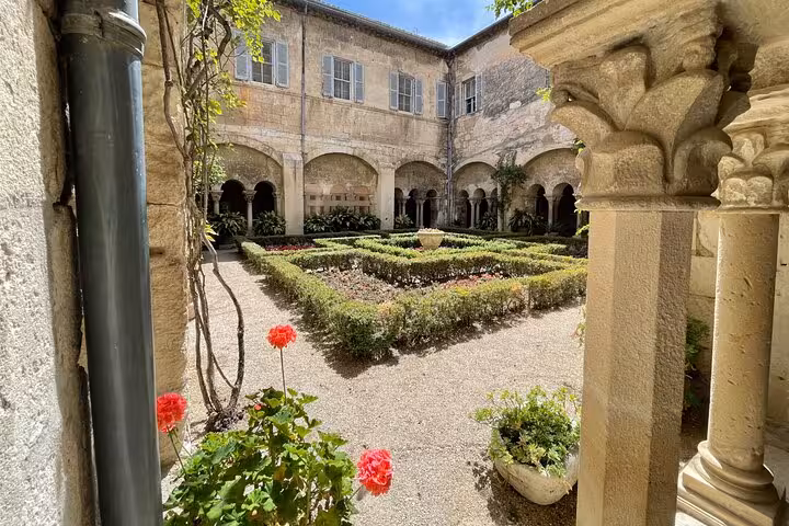 Arles cloister courtyard with carved stone columns, roses and geometric hedges on Provence private day tour