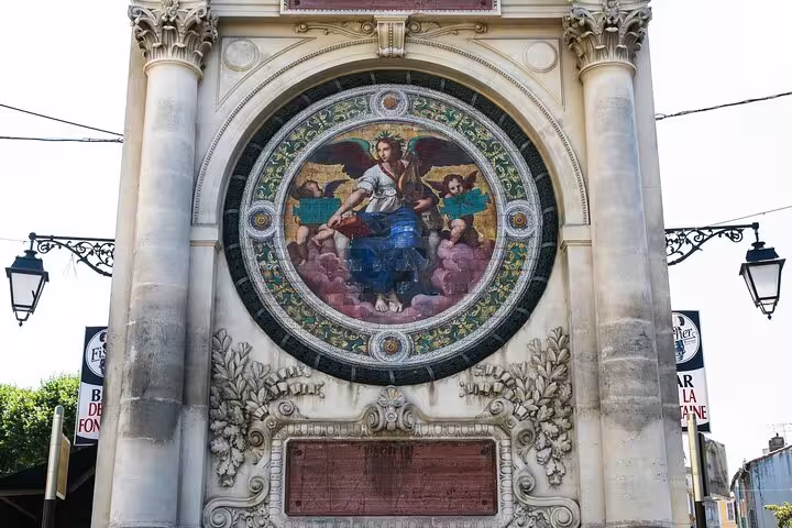Intricate circular mural with classical art and ornate details on a historic structure in Arles.