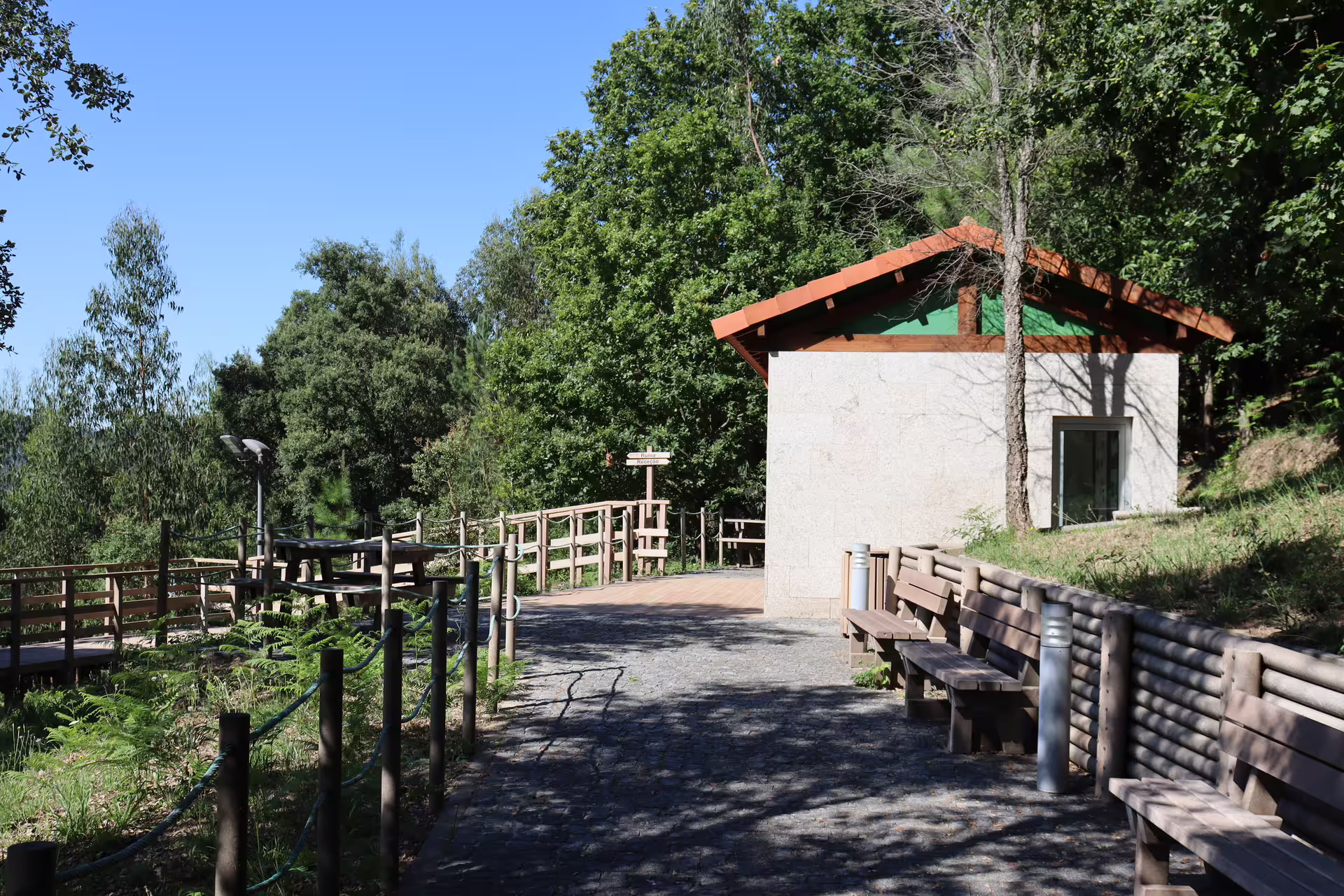 Scenic entrance to Arouca 516 Bridge and Paiva Walkways with lush greenery, wooden benches, and clear blue skies.