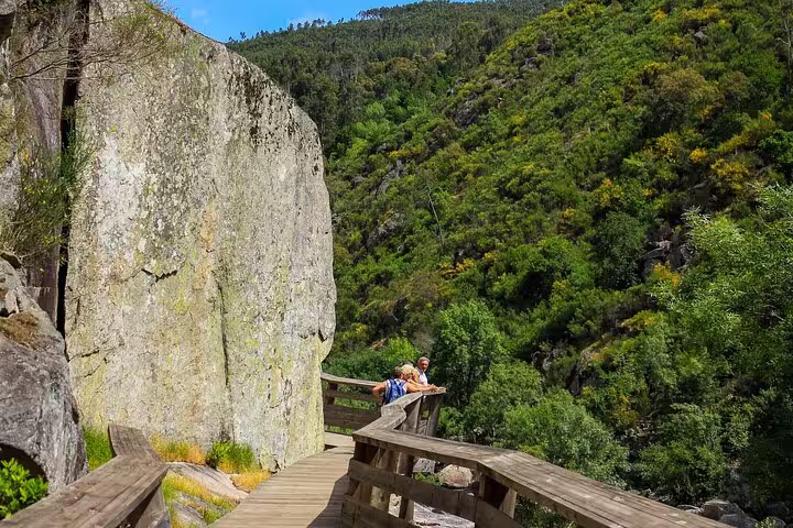 Visitors enjoying a walk along the wooden Paiva Walkways surrounded by lush greenery and rocky cliffs in Portugal.