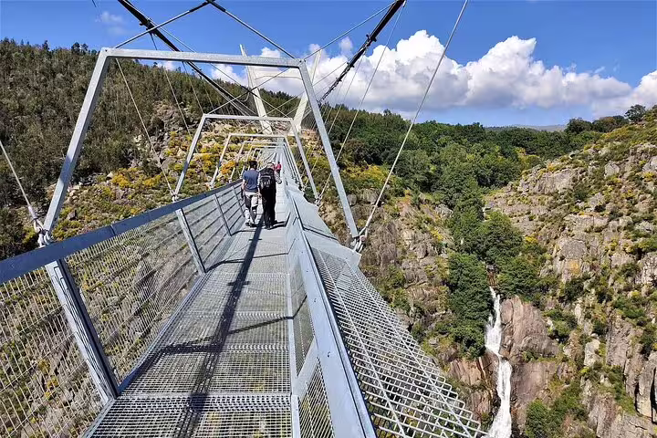 Visitors walking across the stunning Arouca Suspension Bridge, with breathtaking views of the Paiva Walkways and cascading waterfall.