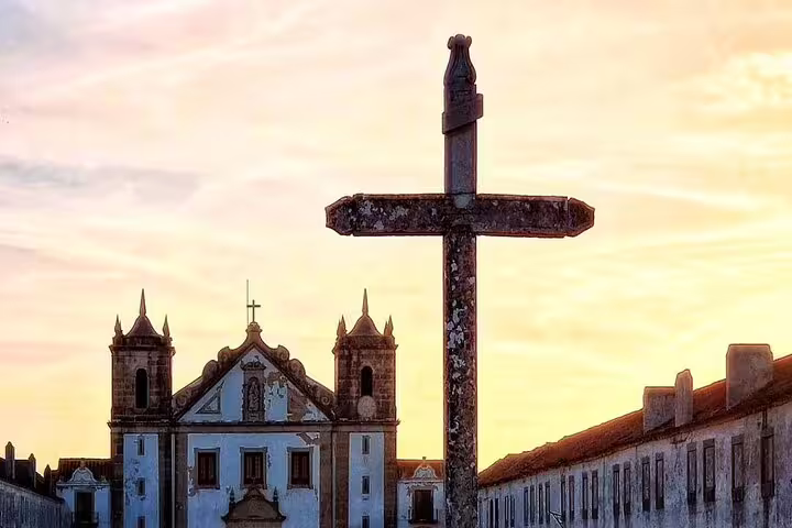 Historic church facade with a stone cross at sunset in Arrábida, capturing the serene beauty of Portuguese architecture.