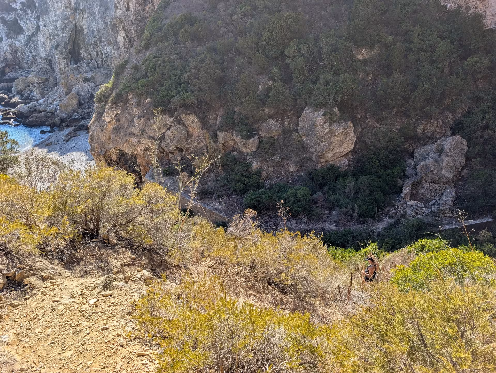 Steep coastal trail above rocky cove on mindful coastal hike, Mediterranean scrub and cliff scenery