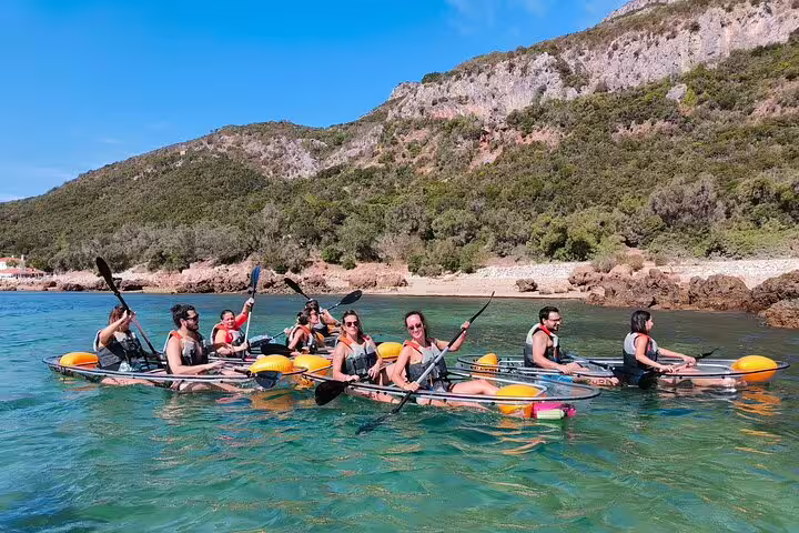 Large group on a guided transparent kayak tour in Arrábida, paddling along lush green hills and calm waters.