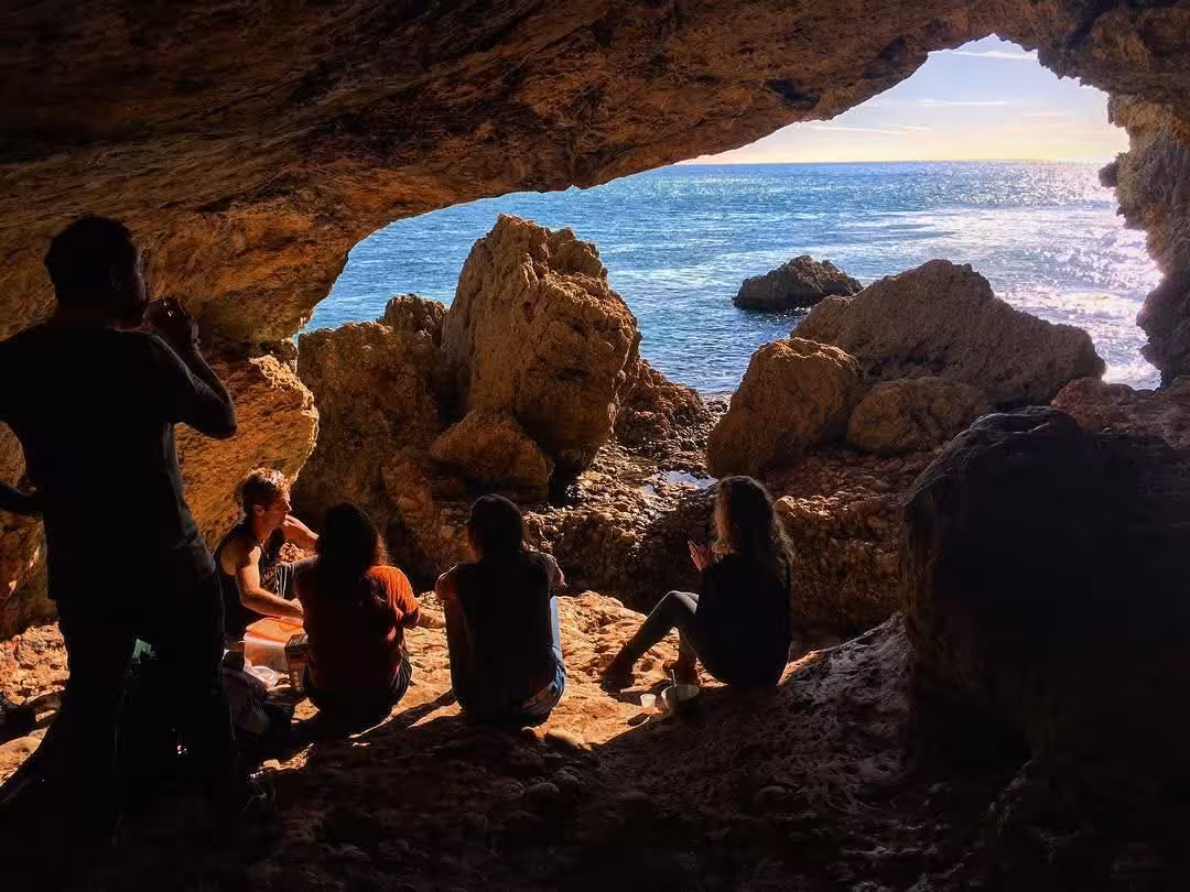 Group relaxing inside a sea cave on Arrábida Safari Tour, overlooking rocky coast and sparkling Atlantic water
