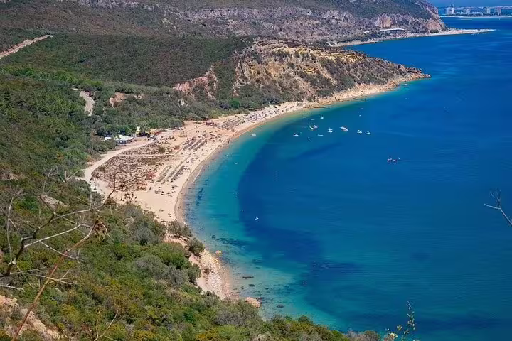Scenic view of a pristine beach along the azure coastline of Arrábida, surrounded by lush greenery, perfect for a nature and wine tasting day trip.