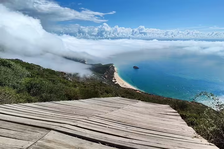 Stunning view of Arrabida's coastline from a wooden boardwalk, showcasing lush greenery and turquoise waters on a day tour from Lisbon.