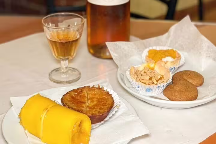 Portuguese pastries and a glass of local wine on a marble table, showcasing culinary delights from the Arrábida & Sesimbra day trip.