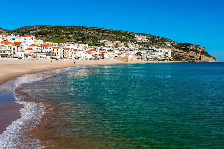Scenic view of Sesimbra's pristine beach with turquoise waters and charming coastal town, ideal for Arrabida wine tasting tour.