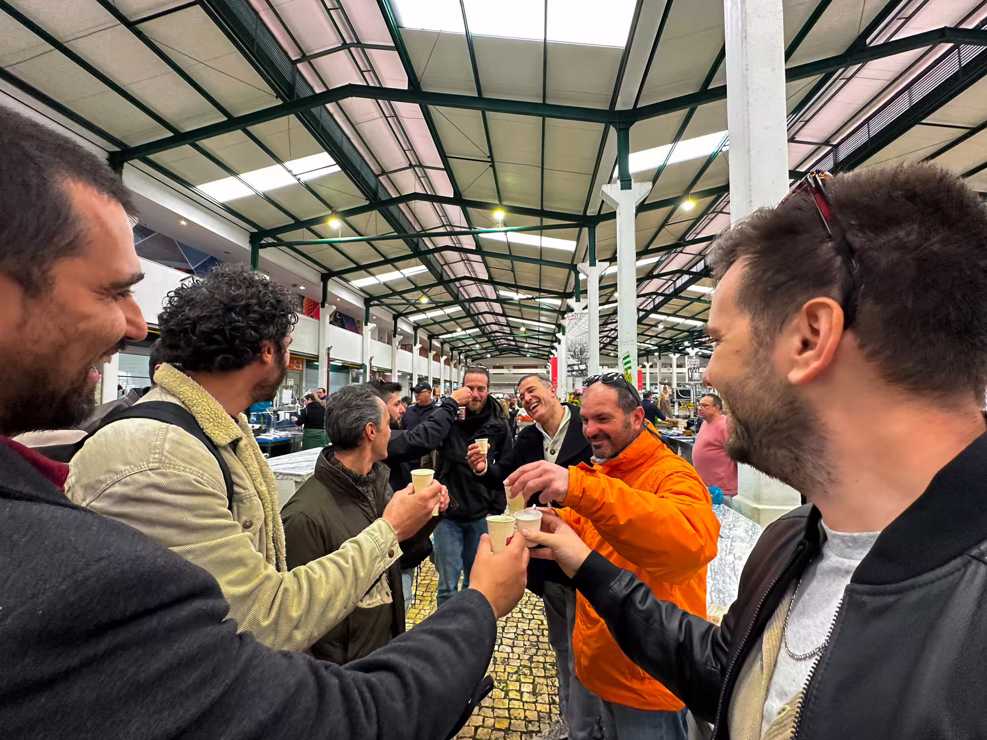 Enjoy a lively group toast in a vibrant, bustling market during the Arrábida and Setúbal private van tour.