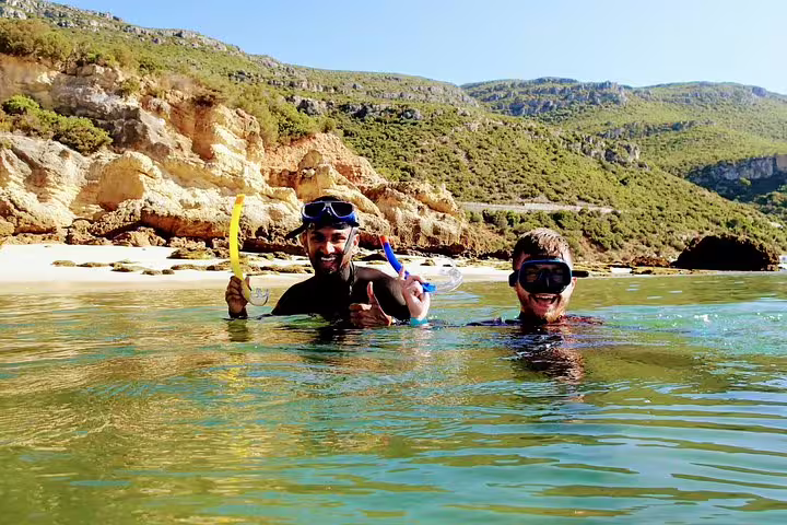 Two snorkelers enjoying the clear waters of Arrábida with scenic cliffs in the background, perfect for a snorkeling and wine tour.