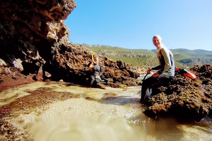 Snorkelers explore rocky tide pools in Arrábida, Portugal, enjoying vibrant marine life and scenic views on a sunny adventure.